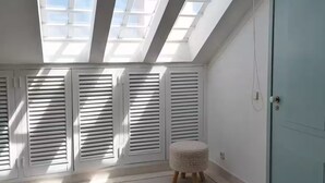 Um quarto com claraboias, uma porta e um pequeno banquinho.