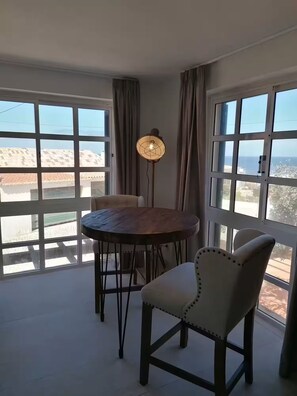A dining area with a round table, two chairs, a floor lamp, and large windows with curtains. - Blue Horizont - Azenhas do Mar (Colares)