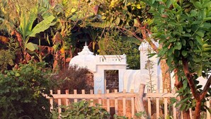 Un jardín con una estructura blanca, posiblemente un mirador, rodeado de exuberante follaje y una valla de madera.