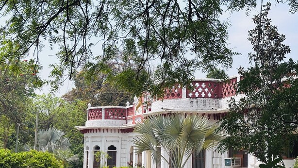 Un edificio tradicional con fachada blanca, detalles en rojo y un balcón con diseño ornamental.