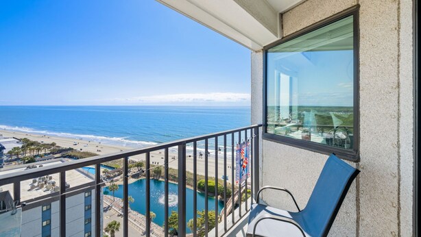 Varanda com vista para o oceano e a praia, piscina e uma cadeira.