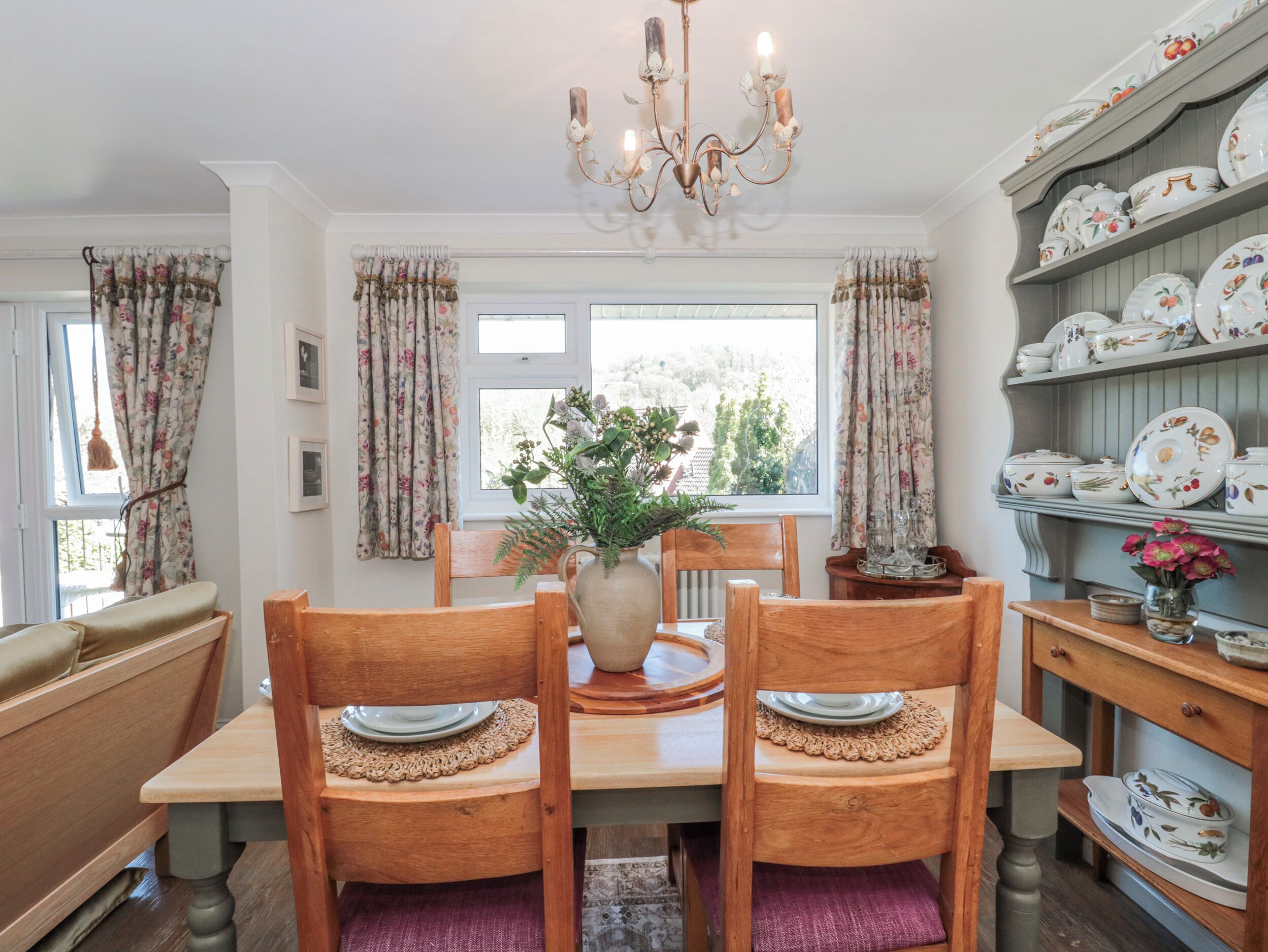 A dining area with a wooden table, chairs, a vase with flowers, and a chandelier.