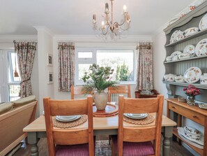 A dining area with a wooden table, chairs, a vase with flowers, and a chandelier. - 7 The Cedars (Wotton-under-Edge)