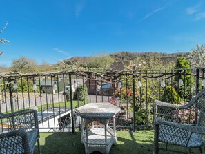 A balcony with wicker furniture, a pergola with hanging lights, and a view of a residential area with houses and greenery. - 7 The Cedars (Wotton-under-Edge)