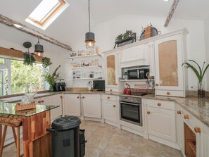 A modern kitchen with white cabinetry, a built-in oven, a microwave, and a glass-top dining table. - 7 The Cedars (Wotton-under-Edge)