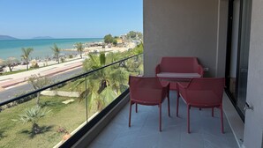 Un balcon avec une table et des chaises, donnant sur une plage et une route.