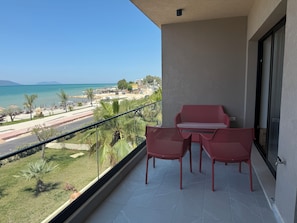 A balcony with a table and chairs, overlooking a beach and road. - Beachfront Apartment (Orikum)
