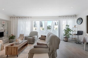 A modern living room with a sofa, armchairs, a coffee table, a TV, and a potted plant.