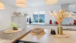 Una cocina moderna con una isla central, luces colgantes y vistas al exterior.