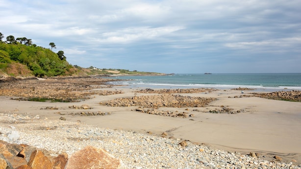 Una playa con terreno rocoso, una orilla de arena y una vista distante del océano.