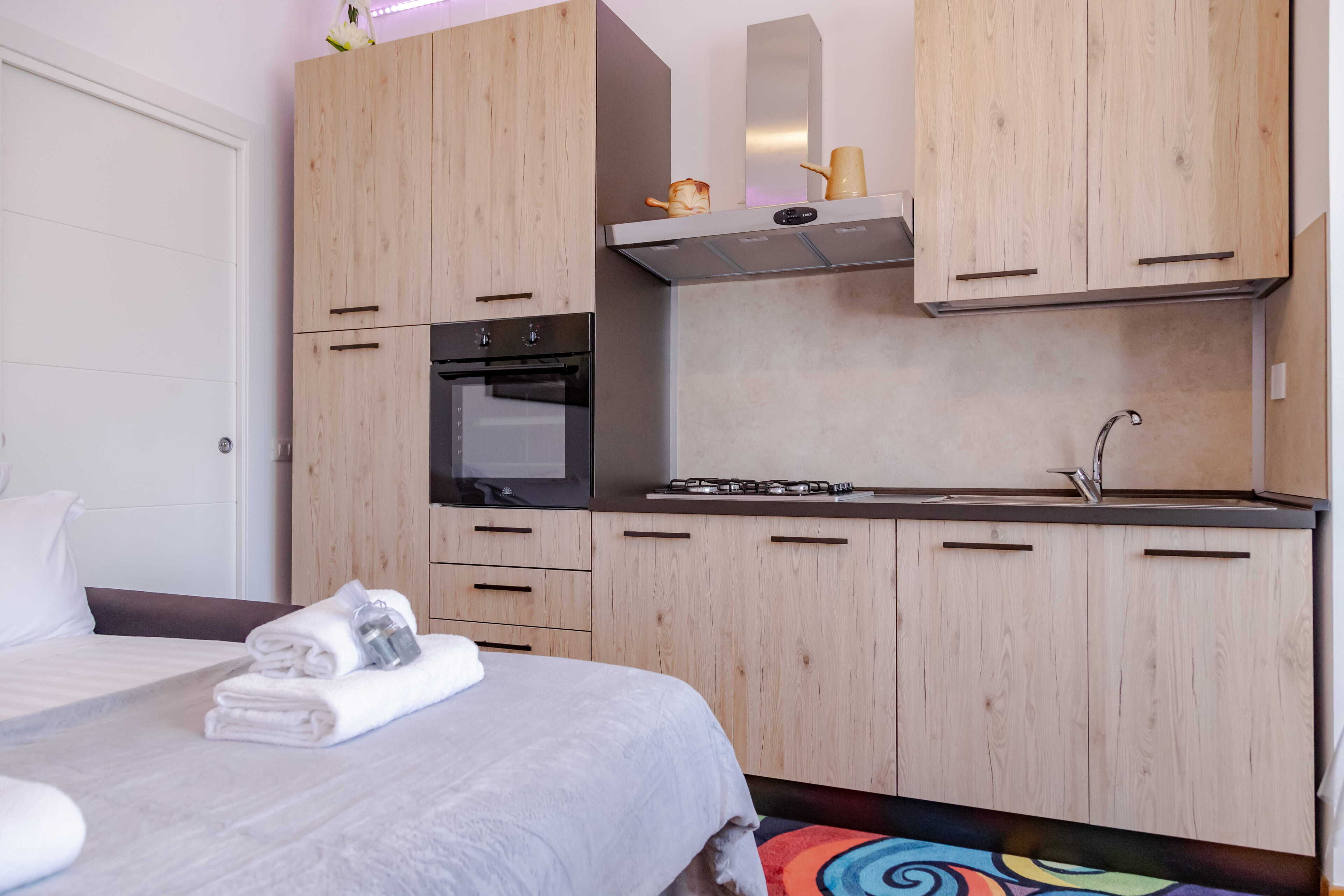 A modern hotel room with a bed, a small kitchenette, and wooden cabinetry.