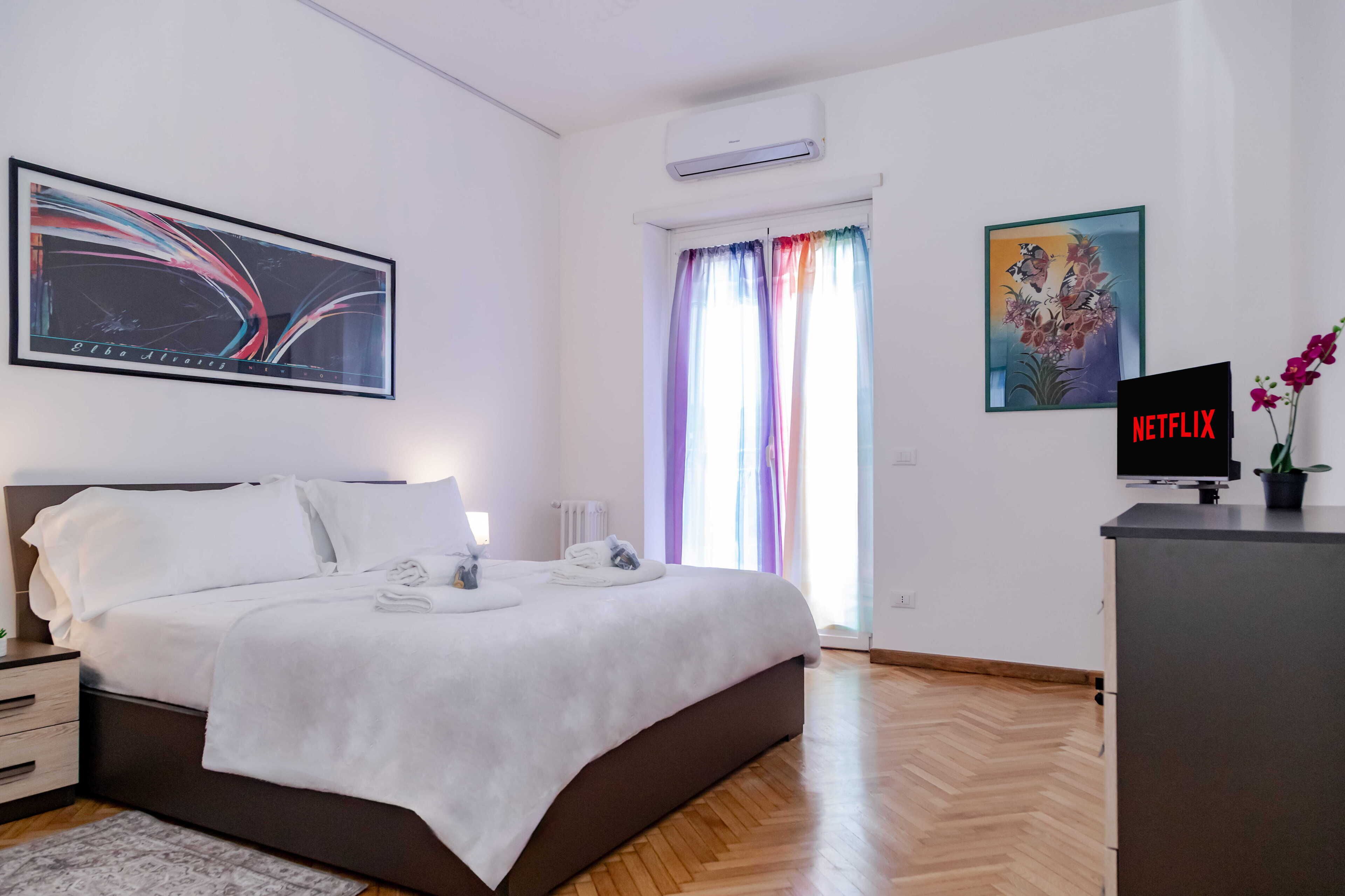Une chambre d’hôtel moderne, équipée d’un lit, d’un bureau avec une télévision et d’une fenêtre avec des rideaux.