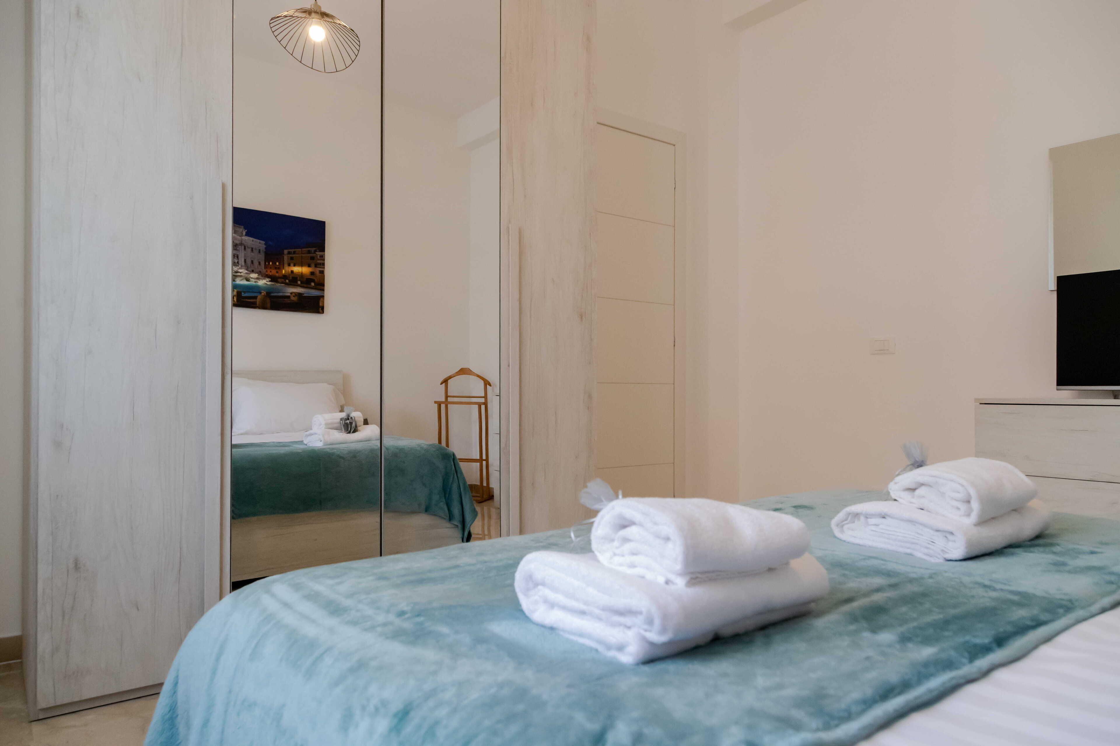 A hotel room with a bed, a mirror, a television, and a door.