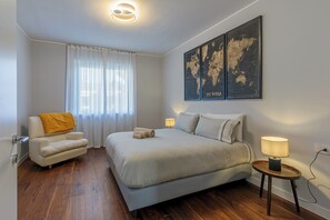 A bedroom with a bed, a chair, a lamp, a world map on the wall, and a window with curtains. - MXP Airport- Villa with Parking -Villa Ceratti -CIN: IT012040C2873Q734M (Cassano Magnago)