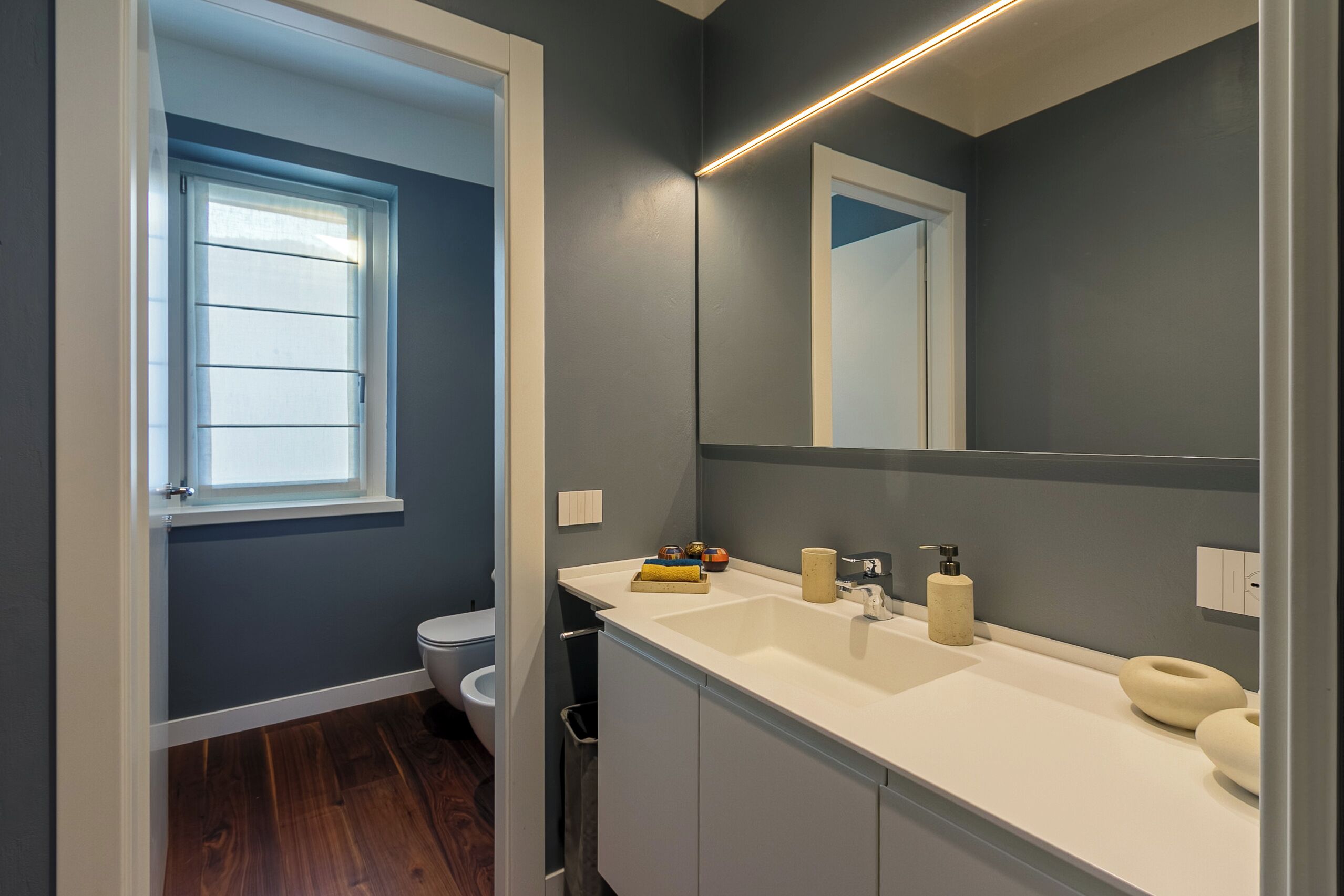 Un baño moderno con un espejo grande, un lavabo blanco y un inodoro.
