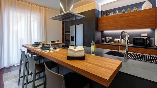 Uma cozinha moderna com ilha central, eletrodomésticos de aço inoxidável e bancada de madeira.