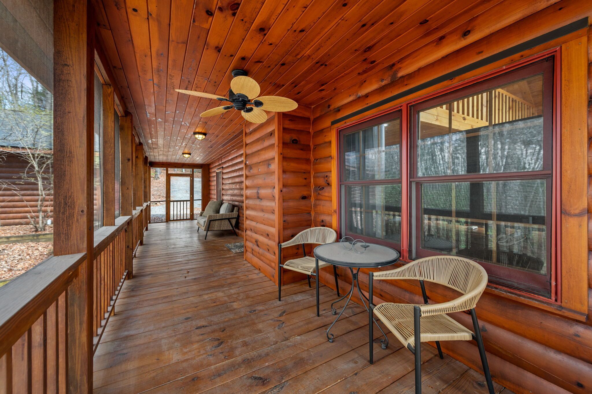 Una baita di legno con veranda, ventilatore a soffitto e tavolo con sedie.