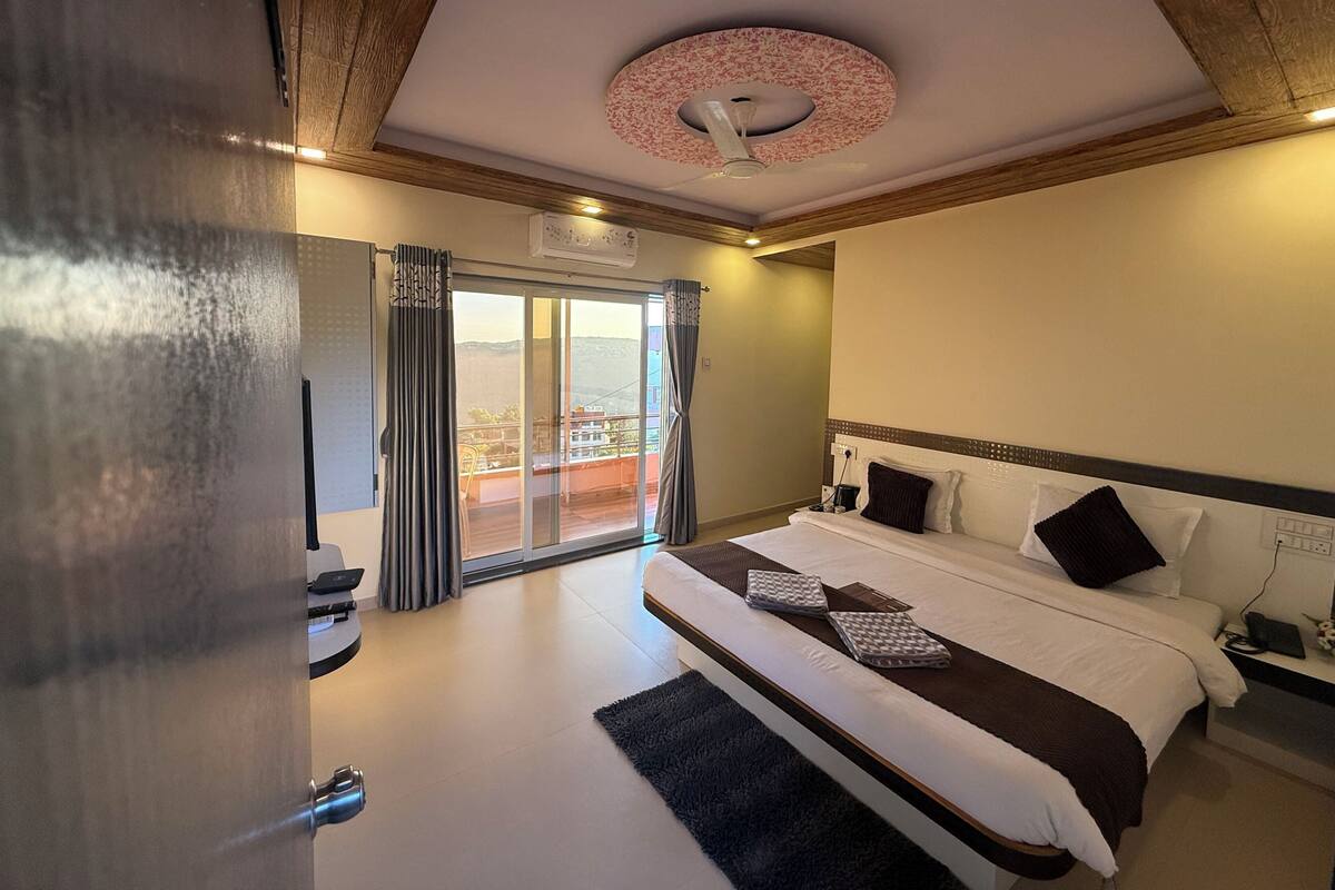 A hotel room with a large bed, a ceiling fan, a view through a sliding door, and a wooden ceiling.