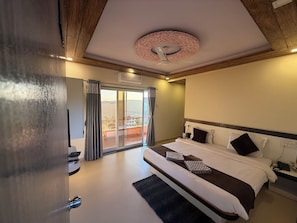 A hotel room with a large bed, a ceiling fan, a view through a sliding door, and a wooden ceiling. - Hotel Mahabaleswer Mount View (Mahabaleshwar)