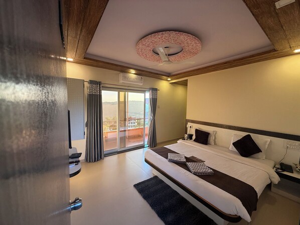 A hotel room with a large bed, a ceiling fan, a view through a sliding door, and a wooden ceiling. - Hotel Mahabaleswer Mount View (Mahabaleshwar)