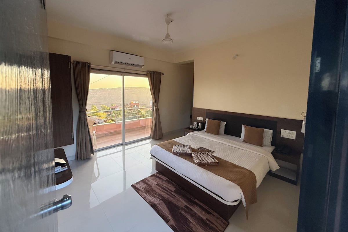 A hotel room with a bed, a nightstand, a window with curtains, and a view of the outside.