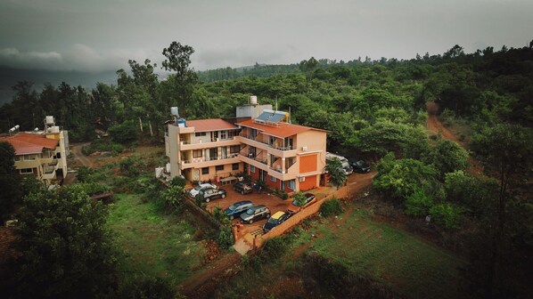 A multi-story building with a parking area and a dirt path leading to it. - Hotel Mahabaleswer Mount View (Mahabaleshwar)