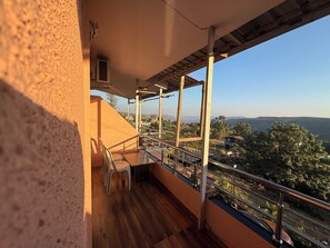 A balcony with a wooden floor, metal railing, and a view of a distant landscape. - Hotel Mahabaleswer Mount View (Mahabaleshwar)