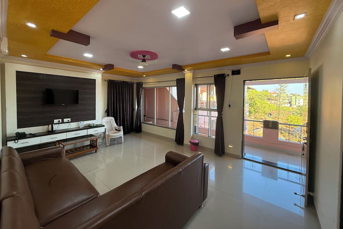 A modern living room with a flat-screen TV, a sofa, a coffee table, and a balcony with a view.