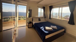 Ein Schlafzimmer mit Bett, Nachttisch, Spiegel, einem Fenster mit Vorhängen und einem Balkon mit Blick.