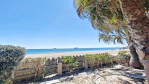 Una playa con palmeras, una valla de madera y un cielo azul despejado.