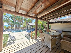 A wooden deck with outdoor furniture, a pool, and palm trees.