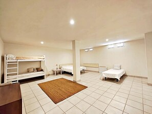 A room with bunk beds, two single beds, a small table, and a brown rug.