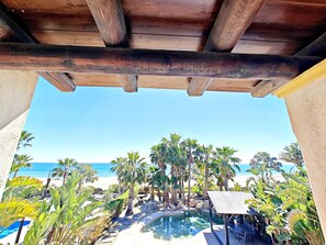 Une pergola en bois surplombant une piscine, avec vue sur une plage et des palmiers.