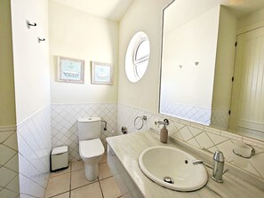 A bathroom with a toilet, sink, and mirror. There are framed pictures on the wall.