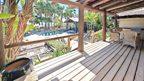Una terraza de madera con piscina, sillas y plantas tropicales.