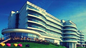 Un moderno hotel a più piani con facciata curva, area salotto esterna e un pendio erboso con decorazioni sferiche colorate.