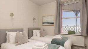 Camera d'albergo con due letti, vista mare, un quadro appeso e una finestra con balcone.