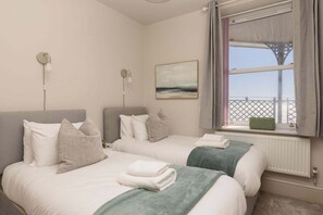A hotel room with two beds, a view of the sea, a painting on the wall, and a window with a view of a balcony.