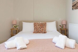 A neatly made bed with white linens, a floral throw pillow, and two bedside lamps.