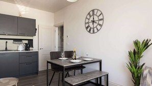 Una cucina moderna con mobili scuri, un tavolo da pranzo con panche, una sveglia a parete e una pianta in vaso.
