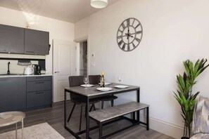 A modern kitchen with dark cabinets, a dining table with benches, a wall clock, and a potted plant.
