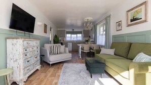 Een woonkamer met een bank, een televisie, een vintage dressoir en een keuken op de achtergrond.