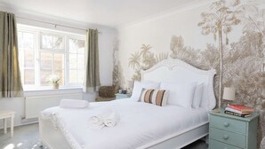Een slaapkamer met een groot bed, een nachtkastje met boeken, een raam met gordijnen en een muur met een tropische muurschildering.