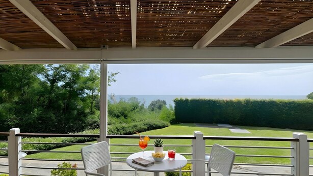 A balcony with a view of a golf course, a table with two chairs, and a small potted plant. - Sea View - 40 Parallelo Mobile Home (Camerota)