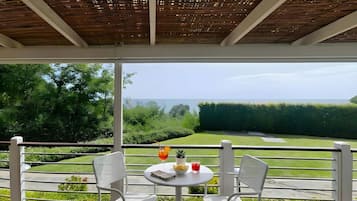 A balcony with a view of a golf course, a table with two chairs, and a small potted plant.