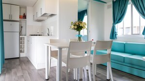A modern kitchen with white cabinets, a dining table with chairs, and a teal sofa. - Sea View - 40 Parallelo Mobile Home (Camerota)