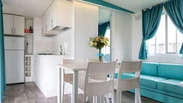 A modern kitchen with white cabinets, a dining table with chairs, and a teal sofa.