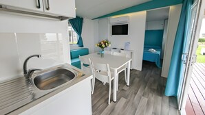 A compact kitchenette with a sink, a dining table with chairs, a small TV, and a blue curtain. - Sea View - 40 Parallelo Mobile Home (Camerota)
