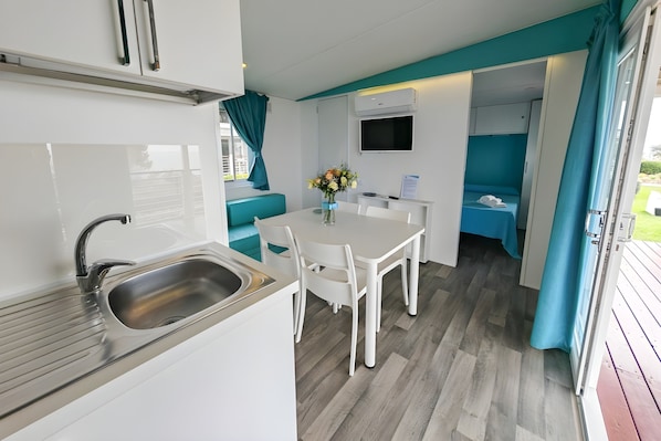 A compact kitchenette with a sink, a dining table with chairs, a small TV, and a blue curtain. - Sea View - 40 Parallelo Mobile Home (Camerota)