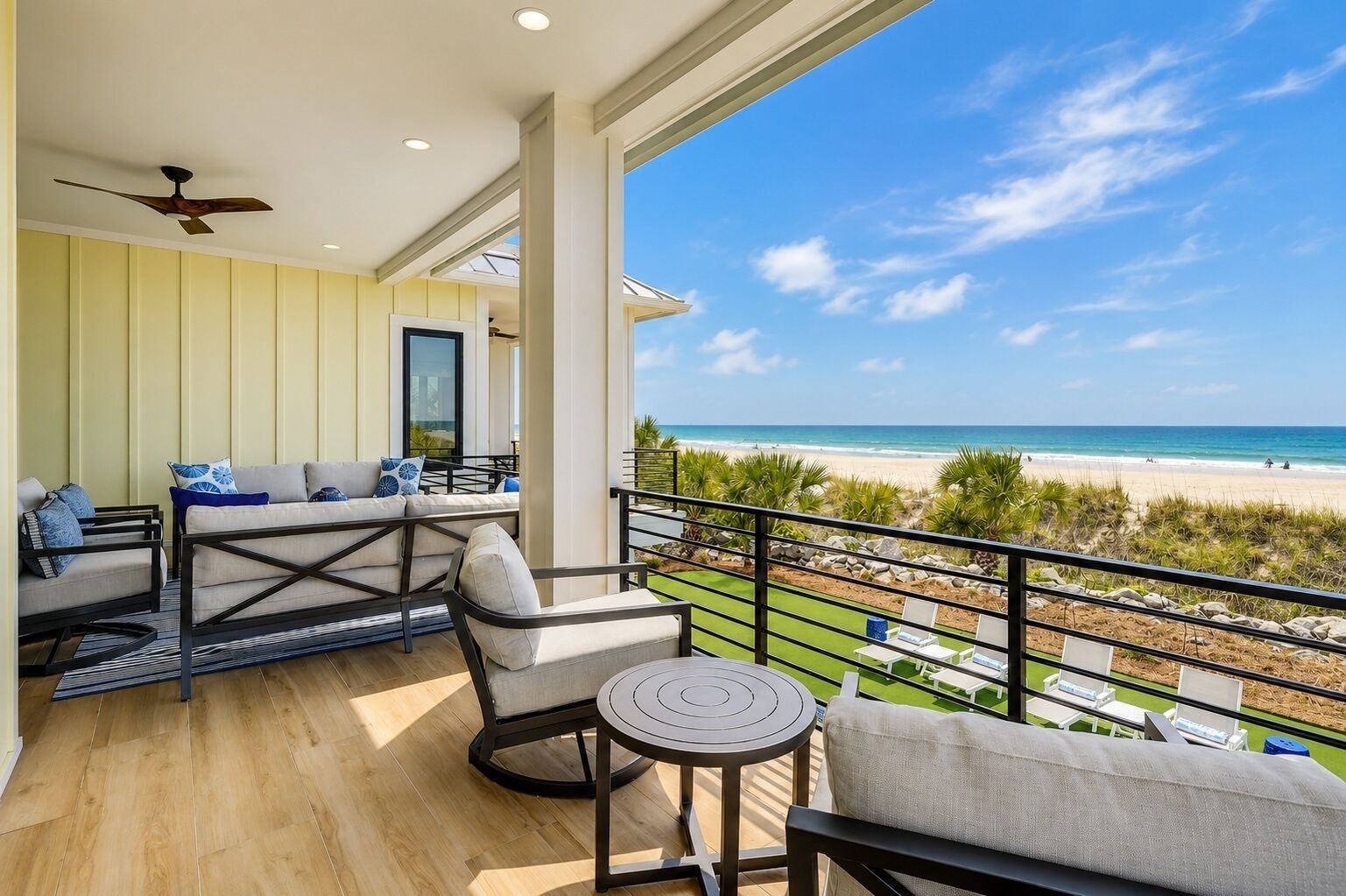 Un balcon avec vue sur la plage, un ventilateur de plafond et un coin salon avec des coussins.
